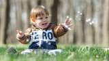 Happy cute smiling baby boy sitting on green grass outdoor playing with soap bubbles. Concept of love, care, parenthood..