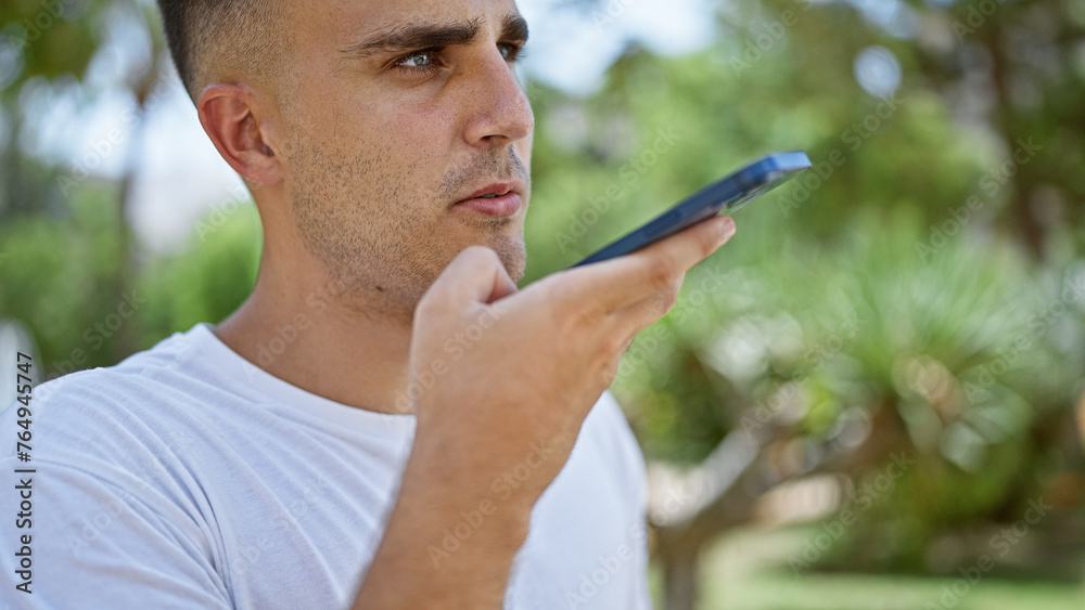 Handsome young man using smartphone outdoors, with focus on face and blurred green background.