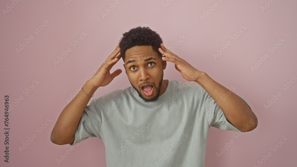 Surprised african american man with hands on head against a pink background, expressing shock or disbelief, portrait. Surprised african american man with hands on head against a pink background, expressing shock or disbelief, portrait.