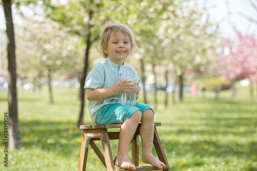 Beautiful blond child, boy, drinking water in the park on a hot day