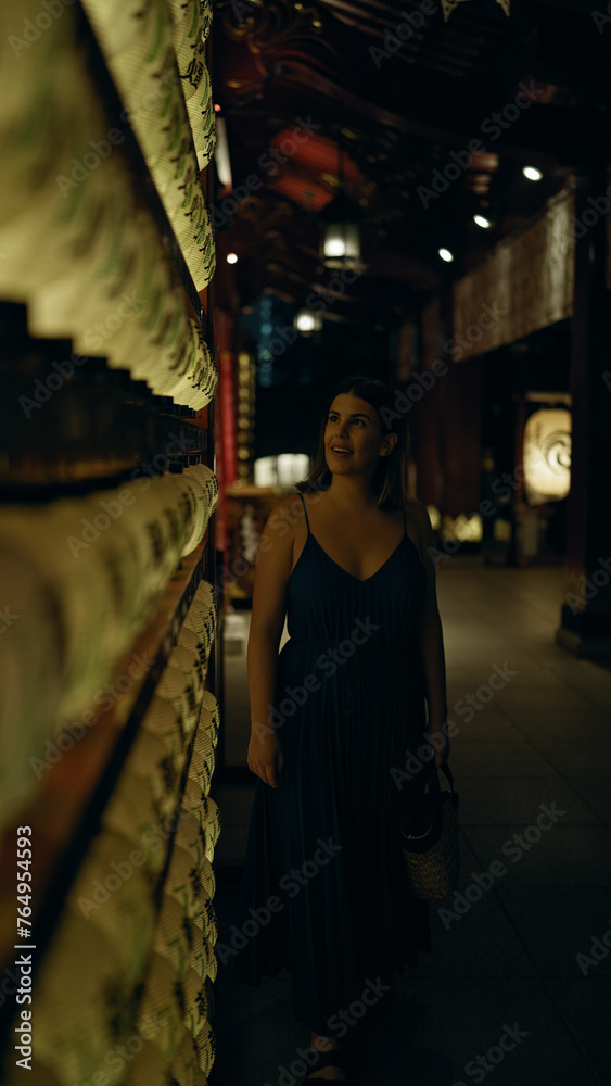 Beautiful young hispanic woman looking at asian lantern at japanese temple in tokyo at night