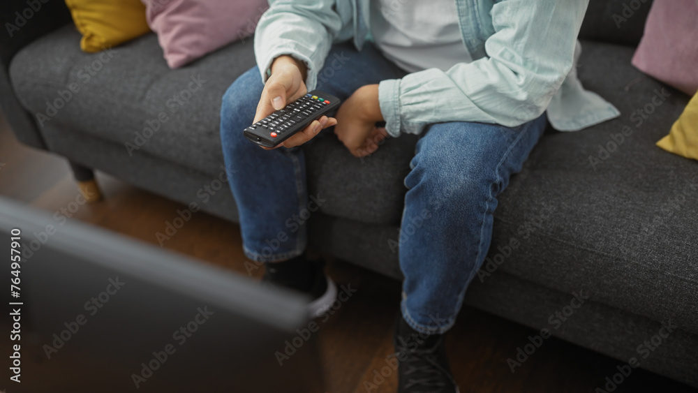 A casual man lounging on a sofa at home holding a remote control, embodying relaxation and domestic life.