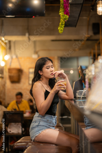 A young woman is sipping a cold alcoholic drink. While sitting at the bar in a rustic cafe and looking at camera.