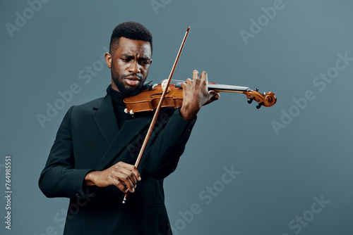 Elegant black violinist in a formal suit performing on violin against a neutral gray backdrop