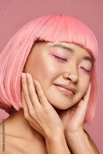 charming woman with pink hair closing eyes and posing with hands against vibrant background