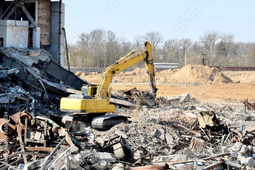 a modern powerful excavator cleans the rubble of a ruined building
