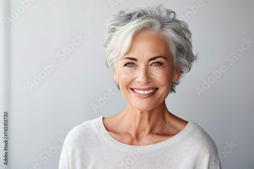 A beautiful smiling senior woman with gray hair and perfect skin in the style of a portrait on a gray background