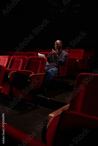 Vertical shot of African American man sitting in audience and reading lines before show in empty theater copy space © Seventyfour