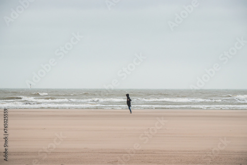 Man walks on a sandy beach in the face of high winds near Blankenberge, west coast of Belgium. Exploring and discovering Belgium