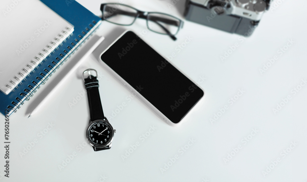 Top view, wrist watch with mobile phone, notebook, eyeglasses and digital camera on white table Top view, wrist watch with mobile phone, notebook, eyeglasses and digital camera on white table