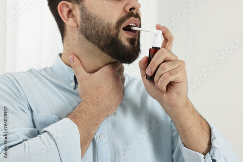 Young man using throat spray indoors, closeup