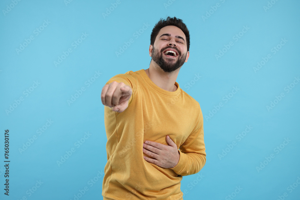 Handsome young man laughing while pointing at something on light blue background Handsome young man laughing while pointing at something on light blue background