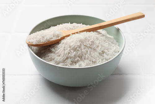 Raw basmati rice in bowl and spoon on white tiled table