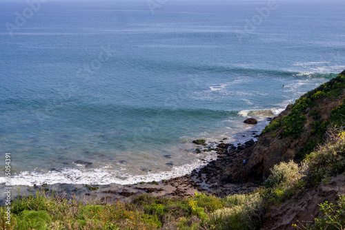 waves rolling into the shore over the rocks with lush green trees and plants and people on the rocks at Point Dume Beach in Malibu California USA © Marcus Jones