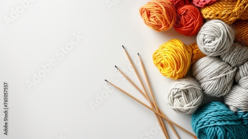Vibrant yellow and red yarn balls beside grey and blue ones, with wooden knitting needles on a white surface.