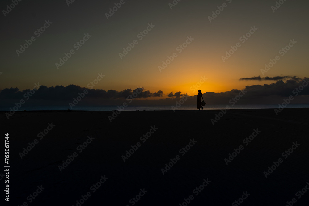 Silhouette of woman holding her hat in her hand in front of the rising sun