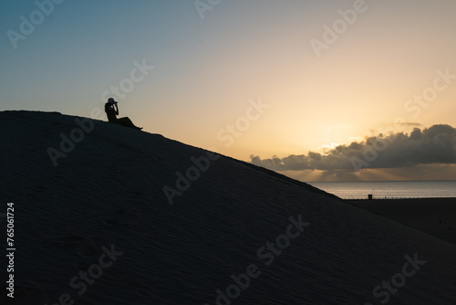 Silhouette of a woman watching the sunrise from the top of a dune.