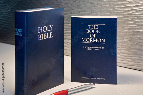 Photos This image shows a Bible and a Book of Mormon, both in dark tones, accompanied by a red and silver pen it is ideal for religious topics, study, and reflection