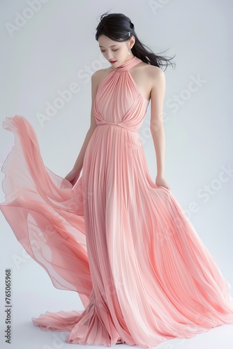 Portrait of a pretty young woman super model of Korean ethnicity draped in an ethereal pink chiffon gown with delicate pleating, a halter neckline, and a flowing train