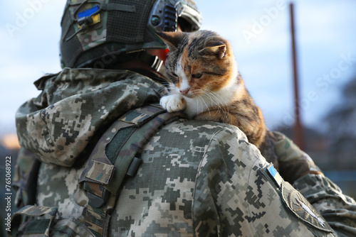Little stray cat on Ukrainian soldier's shoulder outdoors, closeup photo
