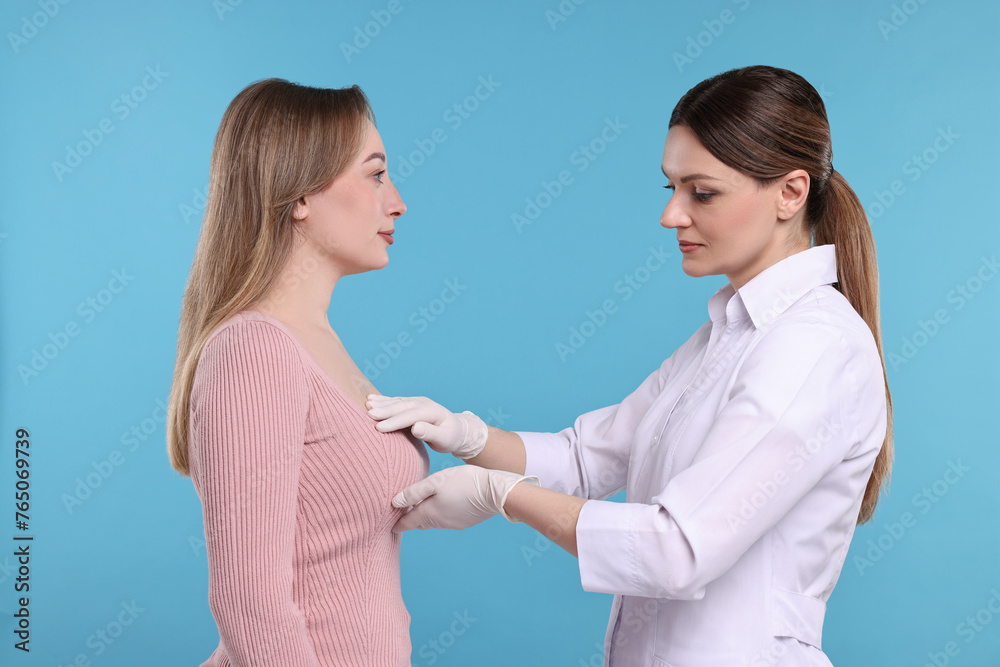 Mammologist checking woman's breast on light blue background Mammologist checking woman's breast on light blue background