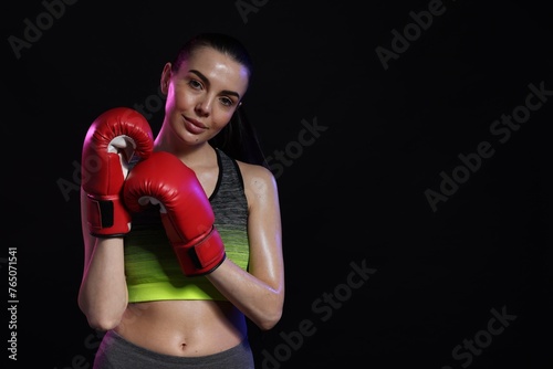 Portrait of beautiful woman wearing boxing gloves in color lights on black background. Space for text