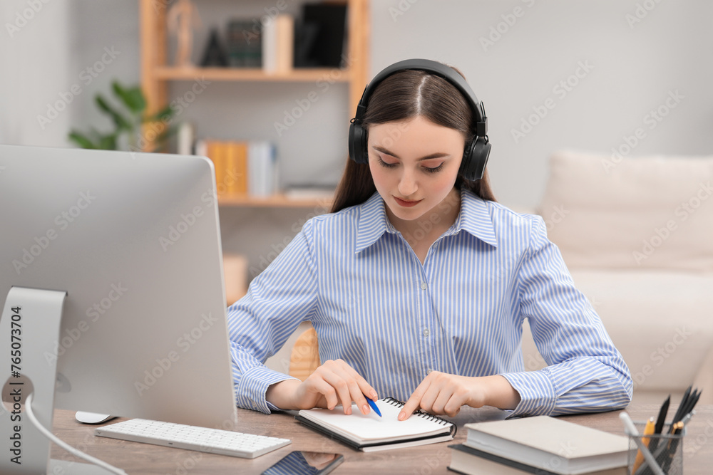 E-learning. Young woman taking notes during online lesson at table indoors E-learning. Young woman taking notes during online lesson at table indoors