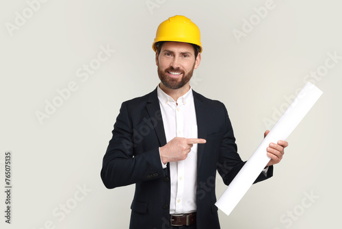 Architect in hard hat pointing at draft on gray background