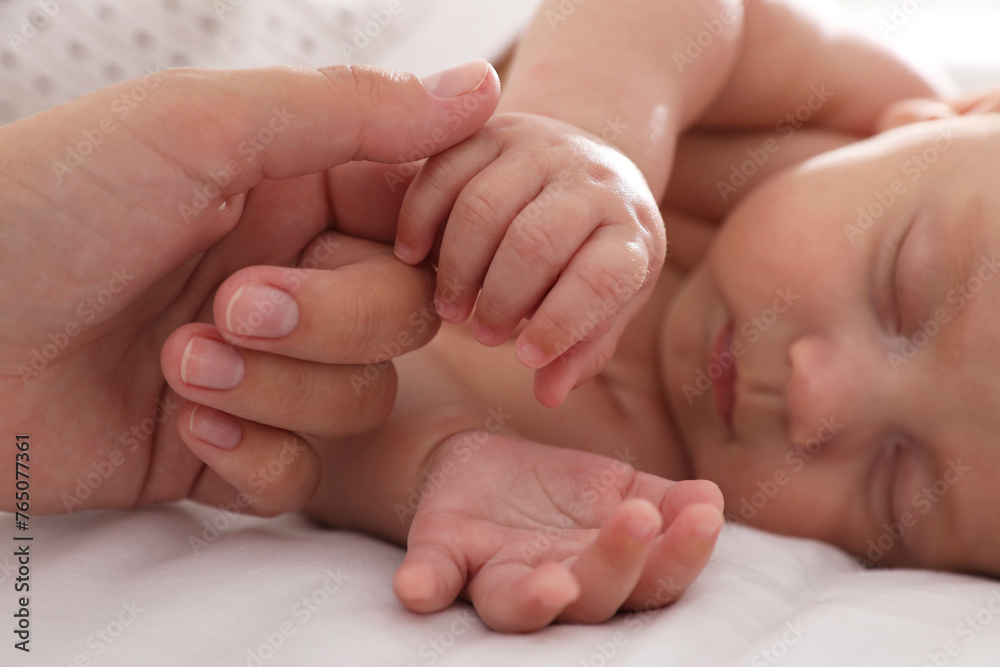 Mother with her cute sleeping baby on bed, closeup of hands Mother with her cute sleeping baby on bed, closeup of hands