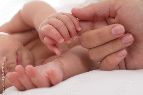 Mother with her cute baby on bed, closeup of hands