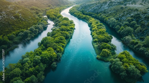 An aerial view captures the winding journey of a river through lush greenery  contrasting with the rocky terrain beside it.
