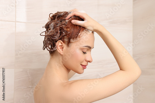 Happy young woman washing her hair with shampoo in shower