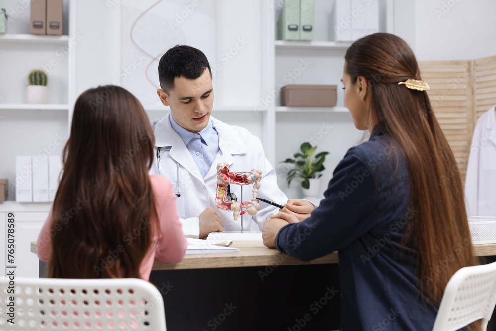 Gastroenterologist with model of intestine consulting woman and her daughter in clinic Gastroenterologist with model of intestine consulting woman and her daughter in clinic