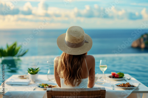 Fototapeta Naklejka Na Ścianę i Meble -  Dinner overlooking the sea in a luxury hotel. A woman in a straw hat sitting at a romantic table overlooking the sea or ocean
