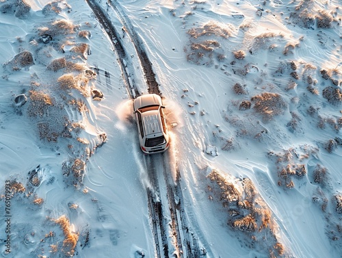 Aerial view of a lone off-road vehicle leaving tracks in fresh snow weaving through a rugged