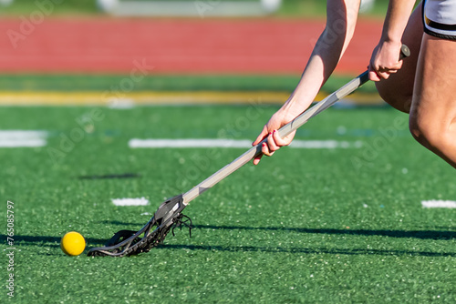 With Spring and Warmer Weather comes Girls Lacrosse to the High School.  Young girls with stick scooping up the yellow ball during a heated game with local rival team in Windsor in Upstate NY. photo