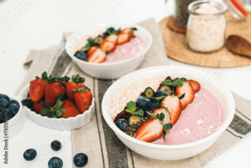 Presented by fruits putting yogurt toppings with strawberry, berry, oats, raisins and chia seed decorated by peppermint in white blow. Pink background. Set of healthy dairy product choice. Pecuniary.