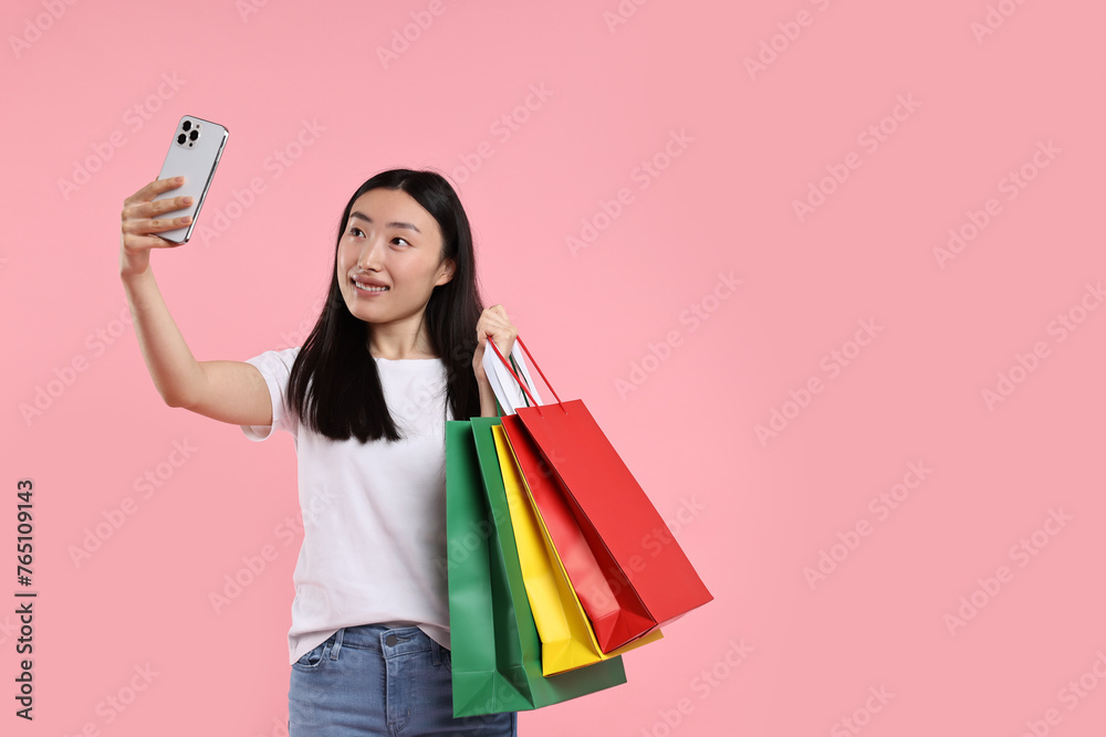 Smiling woman with shopping bags taking selfie on pink background. Space for text Smiling woman with shopping bags taking selfie on pink background. Space for text
