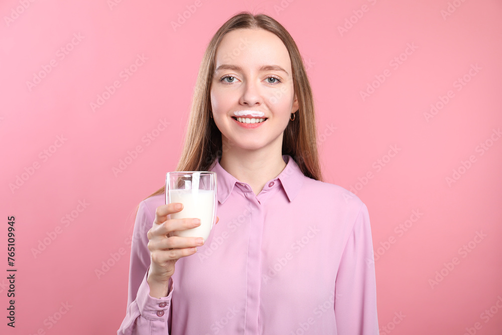 Smiling woman with milk mustache holding glass of tasty dairy drink on pink background Smiling woman with milk mustache holding glass of tasty dairy drink on pink background