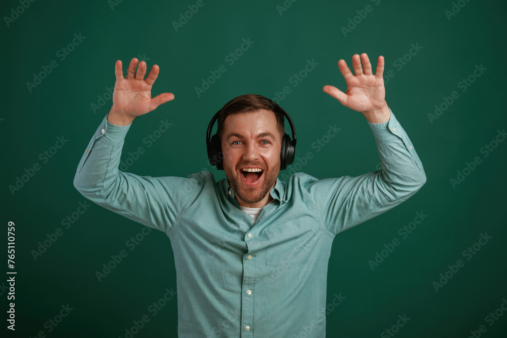 With hands up, in headphones. Man is standing against background in the studio With hands up, in headphones. Man is standing against background in the studio