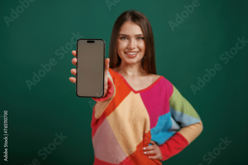 Showing the display of smartphone. Young woman is standing against green background in the studio