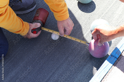Tape measure opened to measure the distance between bocce balls during game to see which color is closer