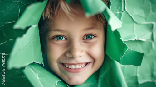 Smiling boy peeking through green torn paper