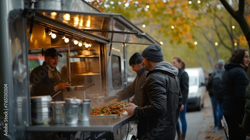 A man in a black jacket and beanie waits in line at a food truck. The truck is lit up by warm lights.
