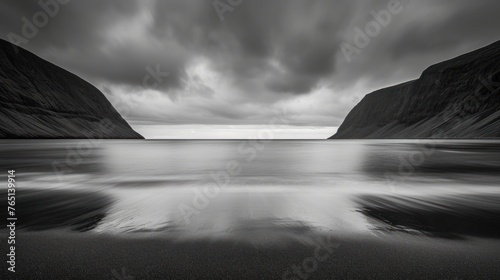 a black and white photo of a body of water with mountains in the background and a cloudy sky above it. photo