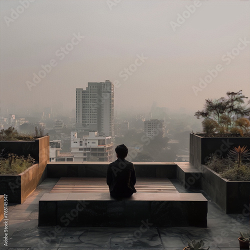 Photography of a lonely man sitting on a rooftop overlooking an urban landscape with a hazy skyline in the background.