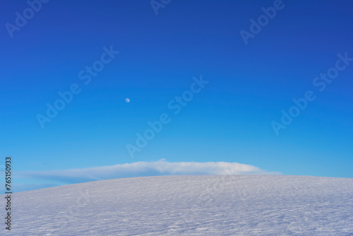 the full moon in the blue sky above a snow covered field