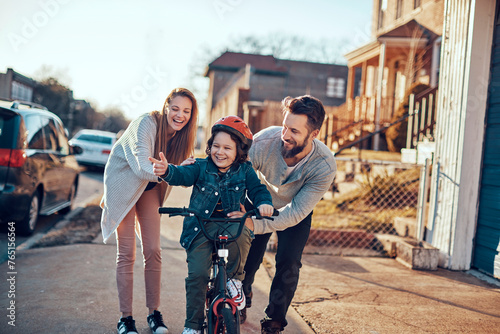 Happy family teaching child to ride a bicycle outdoors