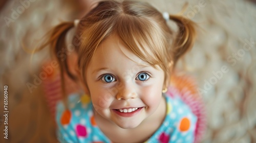Little girl with blond hair and blue eyes smiling. She is wearing a colorful dress with polka dots.
