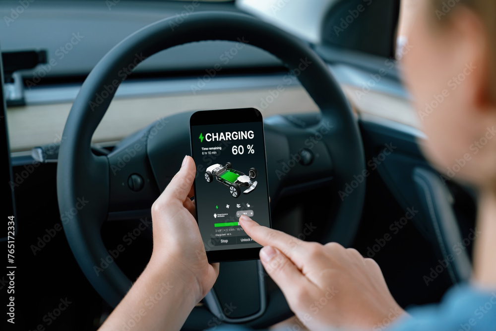 Holiday vacation road trip with environmental-friendly car concept. Eco-conscious woman on driver seat checking EV car's battery status display on smartphone during car travel. Perpetual